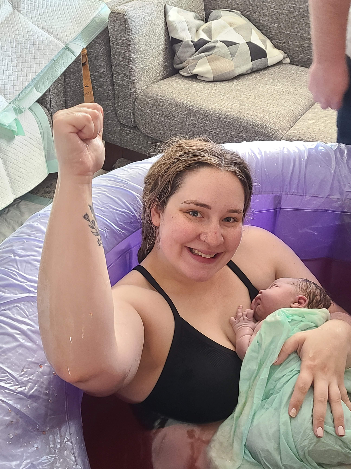 woman holding newborn after waterbirth, holding her arm up in victory